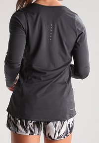 Maglietta sportiva nera a maniche lunghe con tessuto testurizzato e scollatura rotonda. Sei punti riflettenti verticali sulla schiena, abbinati a pantaloni corti con motivo.