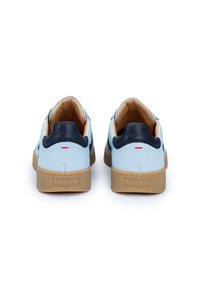 Hellblaue Lederschuhe mit marineblauen Akzenten, strukturierten Gummisohlen und einem kleinen roten Detail an der Ferse. Das Modell zeigt ein Stickmuster.