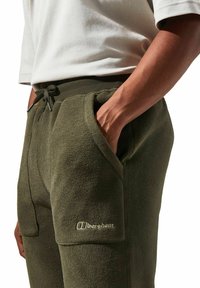 Grüne Fleece-Jogginghosen mit Seitentaschen, elastischem Bund und Kordelzug. Mit Berghaus-Logo in kontrastierender Farbe am linken Oberschenkel.