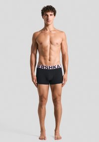 Fekete boxer alsónadrág rózsaszín "BERSHKA" logóval a derékpánton. Az anyag simának, testhezállónak és nyújthatónak tűnik, a kényelem érdekében tervezve.
