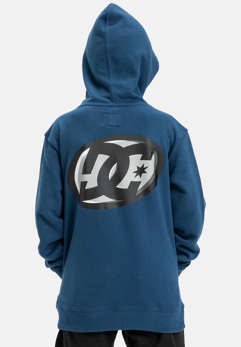 Mikina s kapucňou v tmavomodrom bavlnenom materiáli, na zadnej strane s veľkým čierno-bielym logom. Mäkky materiál, voľný strih a dlhé rukávy.