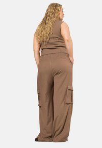 Hnědý dvoudílný outfit s přiléhavým topem bez rukávů a širokými cargo kalhotami, které mají boční kapsy a hladkou texturu.