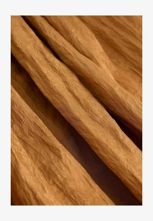 Zkrčená látka v teplom, zemskom hnedom tóne s textúrovaným povrchom, zavesená a prekrývajúca sa v jemných, plynulých záhyboch.