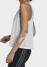 Vitt ärmlöst sportlinne med lös passform, tillverkat av mesh-tyg. Har rundad fåll och en logotyp på vänster axel.