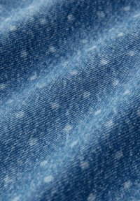 Denim tkanina u srednje plavoj nijansi, s blagim izblijedjelim uzorkom. Tekstura izgleda glatko s blagim tkanjem vidljivim.