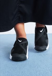 Μαύρα πλεκτά αθλητικά παπούτσια με άσπρες λεπτομέρειες, διαθέτοντας σχέδιο slip-on, υφαντή επιφάνεια και αντίθετο σχέδιο σόλας.