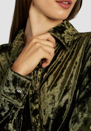 Dunkelgrünes Samthemd mit glänzender Textur, ausgestattet mit einem spitzen Kragen und knöpfbaren Manschetten, akzentuiert durch glänzende silberne Knöpfe.