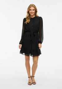 Vestito nero con bottoni frontali, lunghe maniche trasparenti e vita cinturata. Presenta un orlo arricciato e una texture di tessuto leggero.