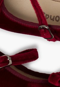 Burgunderrote Samt-Schuhe verfügen über verstellbare Riemen mit silbernen Schnallen, eine flache Sohle und eine weiche, strukturierte Oberfläche. Das Innere ist hell gefärbt.