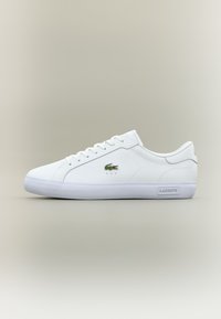 Hvite sneakers laget av glatt lær, med en grønn brodert logo, snøring design og en teksturert gummisåle, med minimale detaljer.