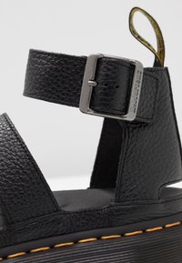 Czarne skórzane sandały z szerokimi regulowanymi paskami, metalowym zapięciem, strukturalnym wykończeniem oraz masywną podeszwą z żółtymi przeszyciami.