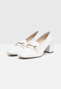 Zapatos loafers blancos con un tacón grueso, presentan un acento de cadena dorada en el empeine, material de cuero suave y un diseño de punta afilada.