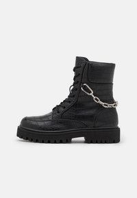 Bota de combate de cuero negro con textura de cocodrilo, cierre de cordones en la parte delantera y detalle de cadena plateada en el tobillo. Suela gruesa y resistente para mayor tracción.