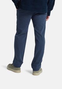 Pantalones azul marino de mezcla de algodón; diseño de pierna recta con una textura suave. Combinados con zapatos de ante grises, parcialmente visibles.