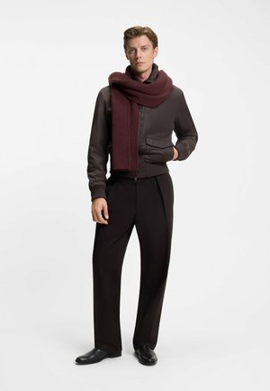 Brown bomber jacket with ribbed cuffs, paired with a maroon ribbed scarf, and black trousers. Model stands in a neutral background.
