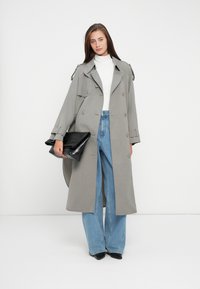 Cappotto grigio con una vestibilità ampia, design doppiopetto e spalline, abbinato a jeans blu a vita alta e una borsa a mano nera.
