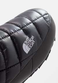 Chausson matelassé isolant noir avec le logo The North Face et une semelle en caoutchouc texturée.