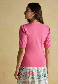 Rosa geripptes Sweatshirt mit gepufften kurzen Ärmeln, das ein tailliertes Design und strukturierten Stoff aufweist. Kombiniert mit einem Rock mit Blumenmuster.