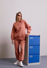 Sudadera de color óxido y joggers a juego, hechos de una tela suave, con un corte relajado. Combinado con zapatillas blancas y gafas de sol elegantes.
