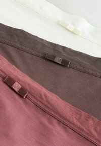 Trois pièces de tissu en crème, marron et mauve, chacune ornée d'un petit nœud cousu le long du bord supérieur.