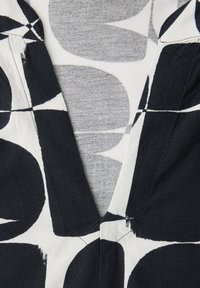 Gros plan sur un tissu à motifs noirs et blancs avec de grandes formes abstraites et un détail d'encolure en V.