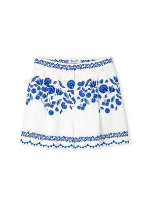 Shorts en lin blancs avec broderies florales bleues, présentant un ourlet festonné et une ceinture à motif. Les plis avant ajoutent de la structure.