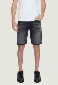 Shorts in denim nero con un leggero sbiadimento, orli arrotolati e chiusura con bottone. Abbinati a sneakers nere e una t-shirt bianca.