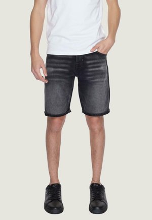 Shorts de mezclilla negra con un ligero desgastado, dobladillos enrollados y cierre de botón. Combinados con zapatillas negras y una camiseta blanca.