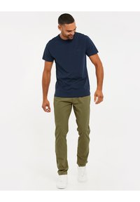T-shirt à col rond bleu marine associé à un pantalon chino vert olive. Présente une coupe décontractée et des baskets blanches. Design minimaliste, tissu lisse.