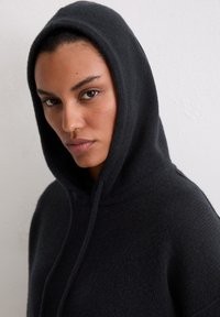 Czarna bluza z kapturem wykonana z teksturowanego materiału o luźnym kroju. Posiada kaptur ze ściągaczem oraz prosty, minimalistyczny design.