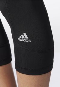 Czarne legginsy sportowe o dopasowanym kroju. Zawierają srebrne logo Adidasa na dolnej części nogawki. Gładki, teksturowany materiał z widocznymi szwami.