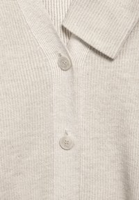 Beige pletený cardigan zblízka, ukazující dva béžové knoflíky a složený límec.