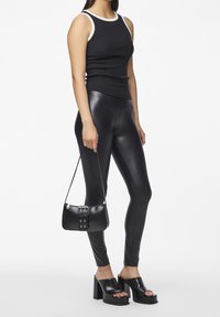 Svart ärmlös topp med vit kant, blanka svarta leggings, svarta plattformssandaler och en liten svart handväska med spänndetalj.
