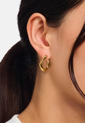 Goldene Creolen mit einer organischen, skulpturalen Form. Glatte, reflektierende Oberfläche mit einem abgerundeten, offenen Design. Am Ohr getragen.