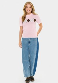 Top a maniche corte di maglia rosa con scollatura tonda, caratterizzato da un motivo a rombi in marrone, blu e bianco. Abbinato a jeans a gamba larga blu chiaro.