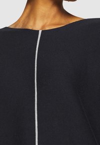 Czarny dzianinowy top z szerokim dekoltem i pionowym białym przeszyciem wzdłuż środka. Miękka tekstura i luźny krój.