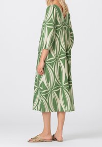 Green midi dress with a V-back, featuring a geometric leaf pattern in cream. Puff sleeves and lightweight fabric. Worn with tan slide sandals.