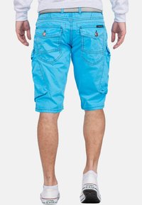 Shorts cargo bleu clair en coton, avec plusieurs poches arrière, une passante pour ceinture et une texture lisse. Portés avec des baskets blanches.