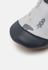 Mīkstas pelēkas ādas kurpes ar jūras zilām akcentiem, ar koku un lāču dizainu, struktūrētu virsmu un noapaļotu purngali.