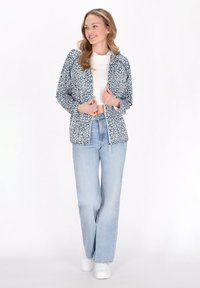 Blå och vit leopardmönstrad zip-jacka med långa ärmar, bärs över en vit topp, matchat med ljusblå jeans och vita sneakers.