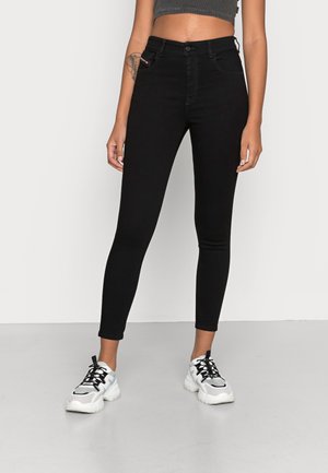 Frau, die hoch taillierte schwarze Skinny-Jeans und weiße klobige Sneakers trägt und vor einem schlichten weißen Hintergrund steht.