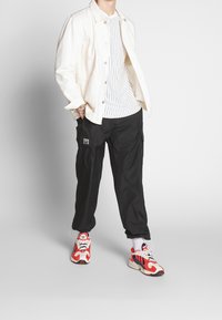 Valkoinen farkkutakki, raidallinen valkoinen t-paita, mustat cargo-housut ja punaiset/valkoiset lenkkarit sinisillä yksityiskohdilla. Rentoa asua vaihtelevilla tekstuureilla.