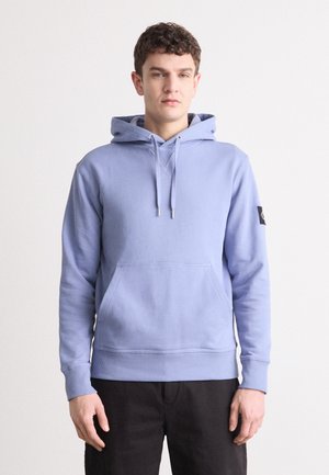 Light blue hoodie made of soft material, featuring a front pocket, drawstrings, ribbed cuffs, and a side patch detail.