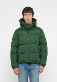 Veste longue en vert avec fermeture éclair à l'avant, capuche et design matelassé. Le matériau semble lisse avec une finition mate et des poignets élastiques.