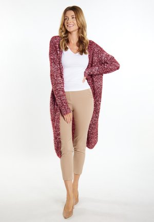 Bordeaux lange cardigan van breiwerk met een textuurafwerking, gecombineerd met een witte V-hals top en beige aansluitende broek, met een relaxte silhouet.