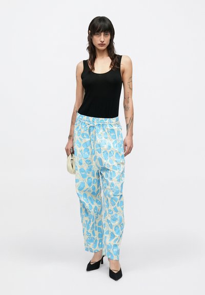 Φωτεινό γαλάζιο παντελόνι με σχέδια και κορδόνι στη μέση, με αφηρημένα σχέδια σε πιο σκούρο μπλε, συνδυασμένο με μαύρο τοπ χωρίς μανίκια και μαύρες γόβες.