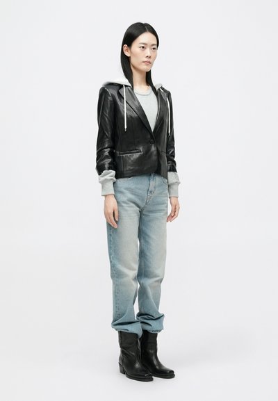 Μαύρο δερμάτινο κοντό μπουφάν με κουκούλα, γκρι πλεκτές λεπτομέρειες, γκρι μπλούζα, ανοιχτό μπλε παντελόνι ίσιας γραμμής και μαύρες μποτάκια.