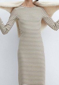 Kerman, pitkähihainen, vaaleancreme mekko, jossa on mustia vaakaraitoja. Mekossa on pyöreä kaula-aukko ja tiukka siluetti, jota korostaa pehmeä, kevyt wrap.