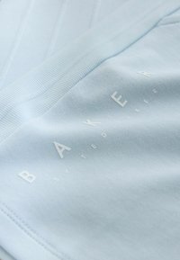 Jasnoniebieska tkanina o subtelnej prążkowanej fakturze, z białym logo "BAKER by TED BAKER" umieszczonym ukośnie.