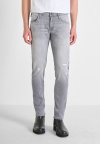 Jeans de denim gris con corte slim, con detalles desgastados y diseño de cinco bolsillos. Combina con botas negras hasta el tobillo.